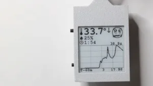 Handheld data logger display showing temperature 33.7°, downward arrow, 25% humidity, and a small graph on the screen.