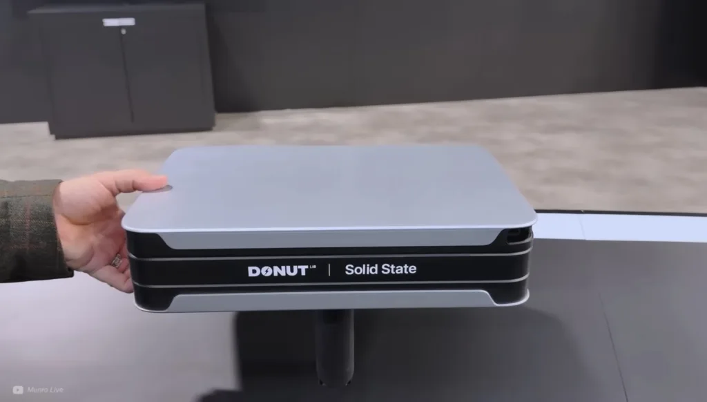Hand holding a compact Donut Lab Solid State device with a light gray top and black base, logos visible.