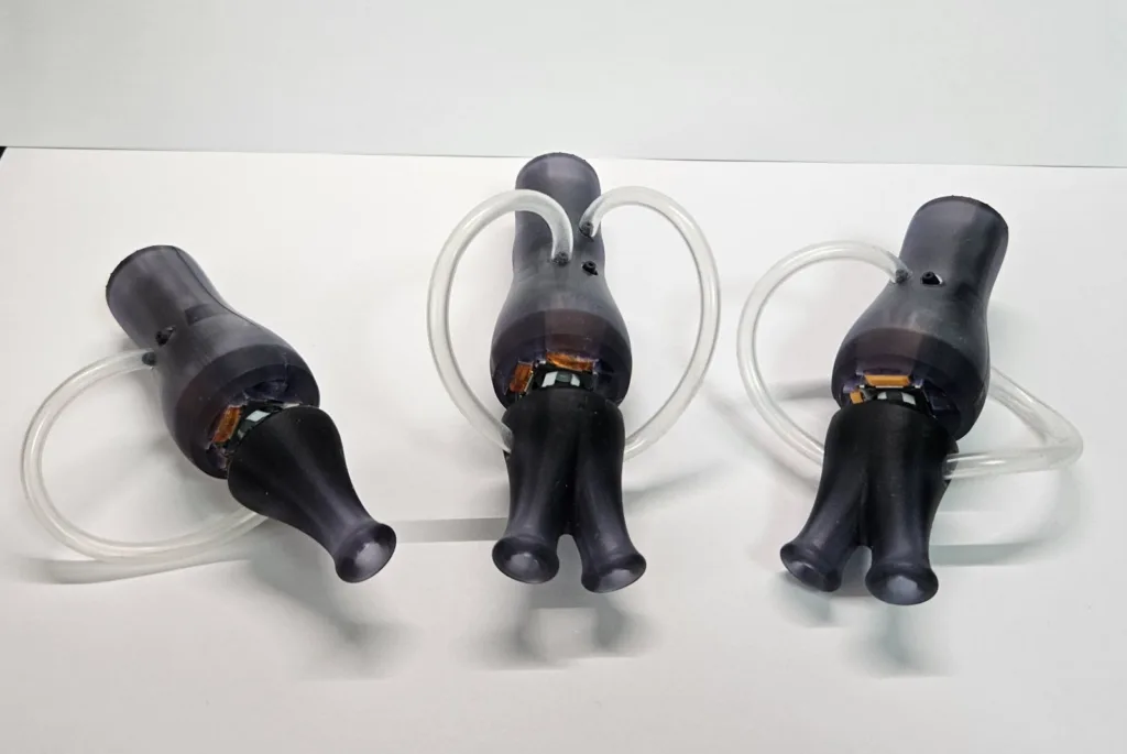 Three black medical-style breathing masks attached to clear flexible tubes, laid on a white surface.