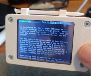 Small white handheld device with a blue screen showing a Frankenstein passage, held by a person.