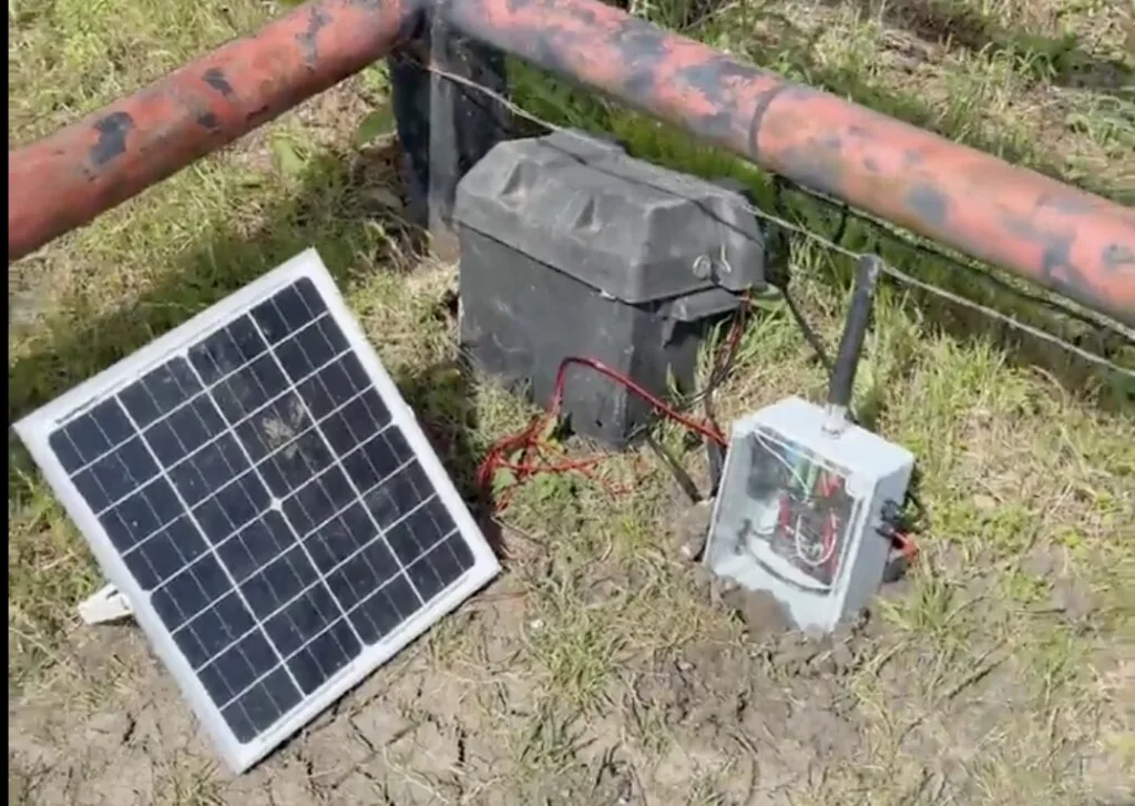 Outdoor off-grid power setup: a solar panel connected to a battery box and a metal control box on muddy ground.