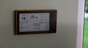 Wall-mounted wooden-framed digital calendar displaying Monday the 16th, weather icons, and upcoming events.