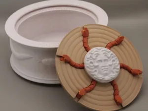 Abstract sculpture with beige concentric discs and orange segmented tentacles wrapping a white textured center on a gray surface.