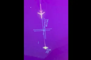 Infrared image showing a small airplane icon aligned with a vertical axis and crosshair marks against a purple background, suggesting a targeting/alignment display.