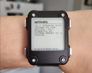 Smartwatch on a wrist showing a dictionary entry for 'spirituality' on its screen: 'n. concern with things of the spirit; n. property or income owned by a church'