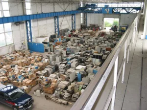 Warehouse filled with old appliances and boxes under a blue overhead crane spanning the space on a cluttered floor plan.
