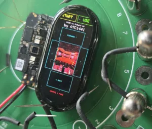 Close-up of a smartwatch-like device on a green circuit board, displaying a menu with START and USE and the line 'by ATC1441'.