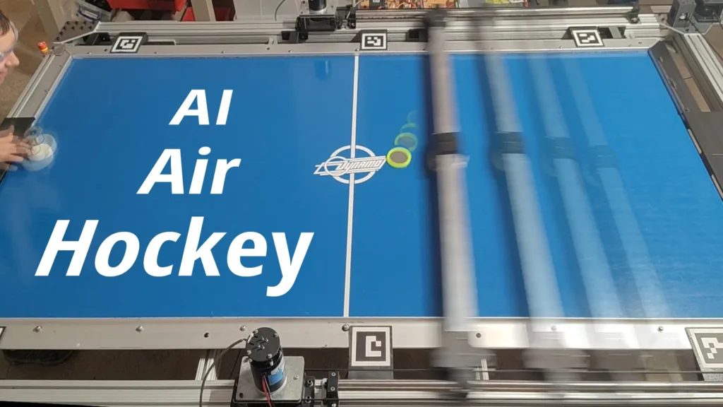 Blue air-hockey table surface with large white text 'AI Hockey' and a logo, surrounded by robotic machinery and rails.