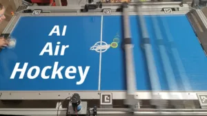 Blue air-hockey table surface with large white text 'AI Hockey' and a logo, surrounded by robotic machinery and rails.