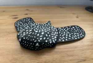 Black, wing-shaped device with a white polka-dot pattern on a wooden surface.