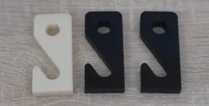 Close-up of three plastic brackets with circular holes, white on the left and two black on the right, laid on a light wood surface.