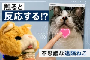 A plush orange stuffed toy taps a photo of a cat on a screen with a glowing pink heart, overlaid with Japanese captions.
