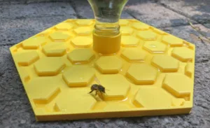 Yellow hexagonal-patterned plastic base with a central nozzle and a bee on it.