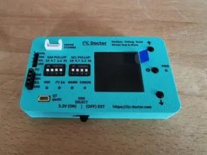 Turquoise I2C Doctor device with LCD screen and labeled SDA/SCL pull-up pins for analyzing and debugging I2C buses.
