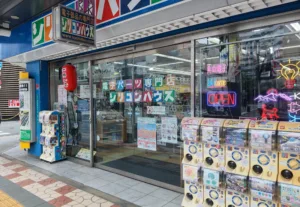 Front of a Japanese electronics storefront with colorful signage in the window, a red lantern hanging outside, and bright neon 'OPEN' and 'Welcome' signs in the display window.