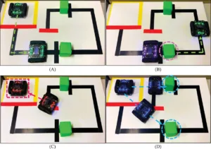 Two small robots navigate a white maze with black walls; a green block and red barrier are present, with a dashed green route shown. The scene suggests a planned path.