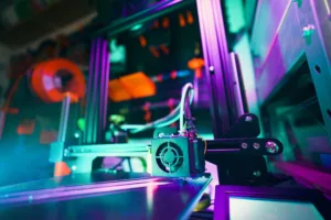 Close-up of a neon-lit industrial machine with cables, gears, and metal framework under colorful LED lighting.