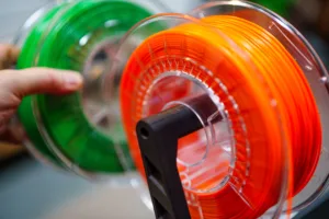 Close-up of orange and green 3D printer filament spools mounted on a reel, ready for printing.